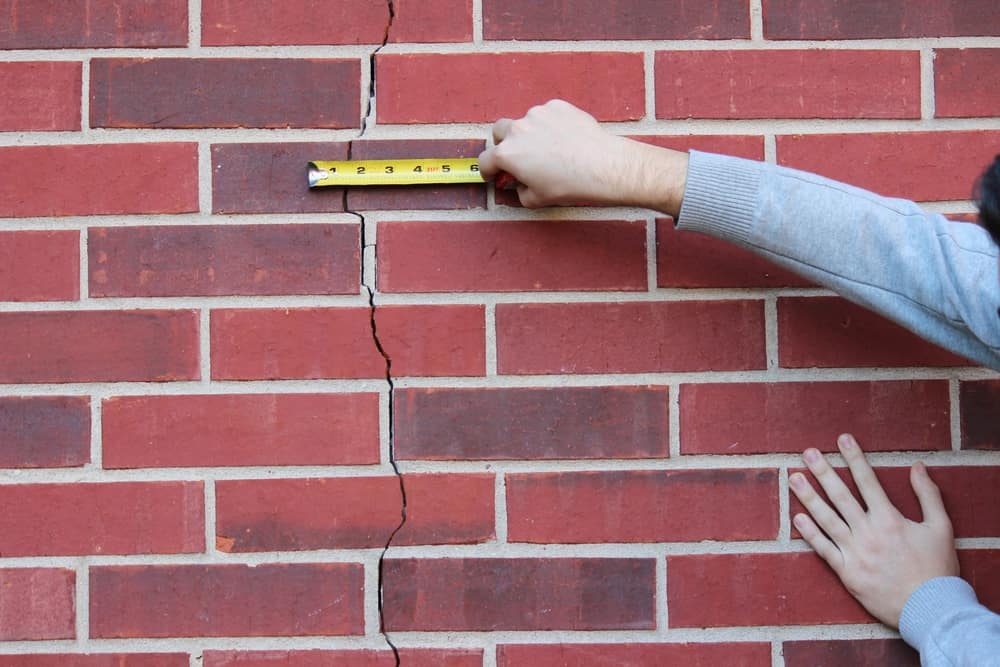 Hands Pointing To A Crack In Brick wall